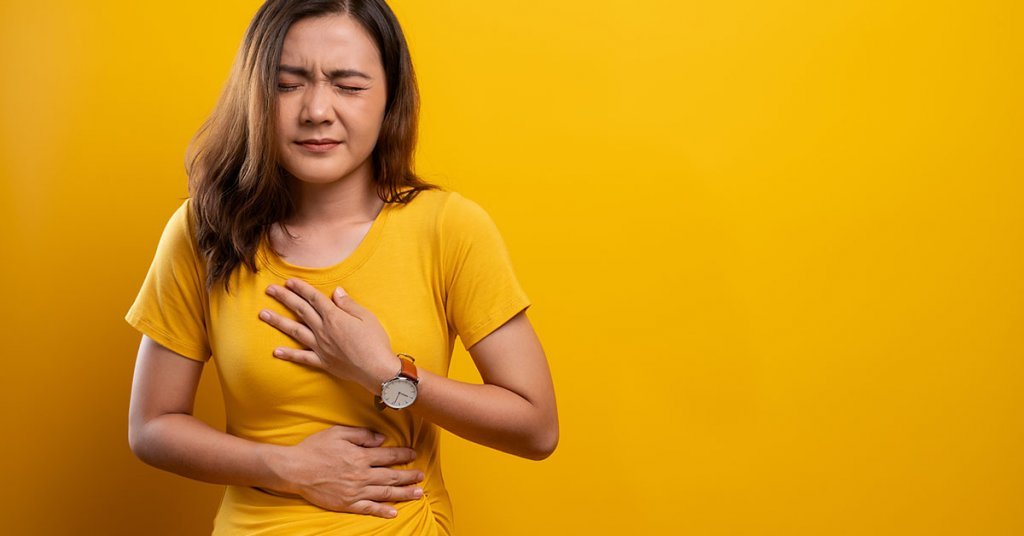 Woman has stomachache isolated over yellow background; blog: Hiatal Hernia Symptoms & Treatments