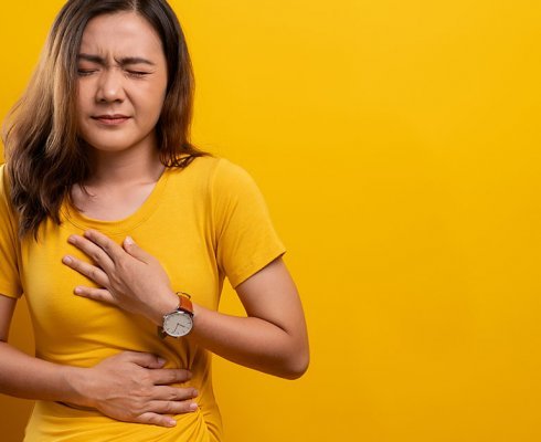 Woman has stomachache isolated over yellow background; blog: Hiatal Hernia Symptoms & Treatments