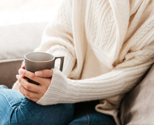 A woman wearing a sweater holding a warm cup of tea to represent wintertime tips for gastrointestinal health
