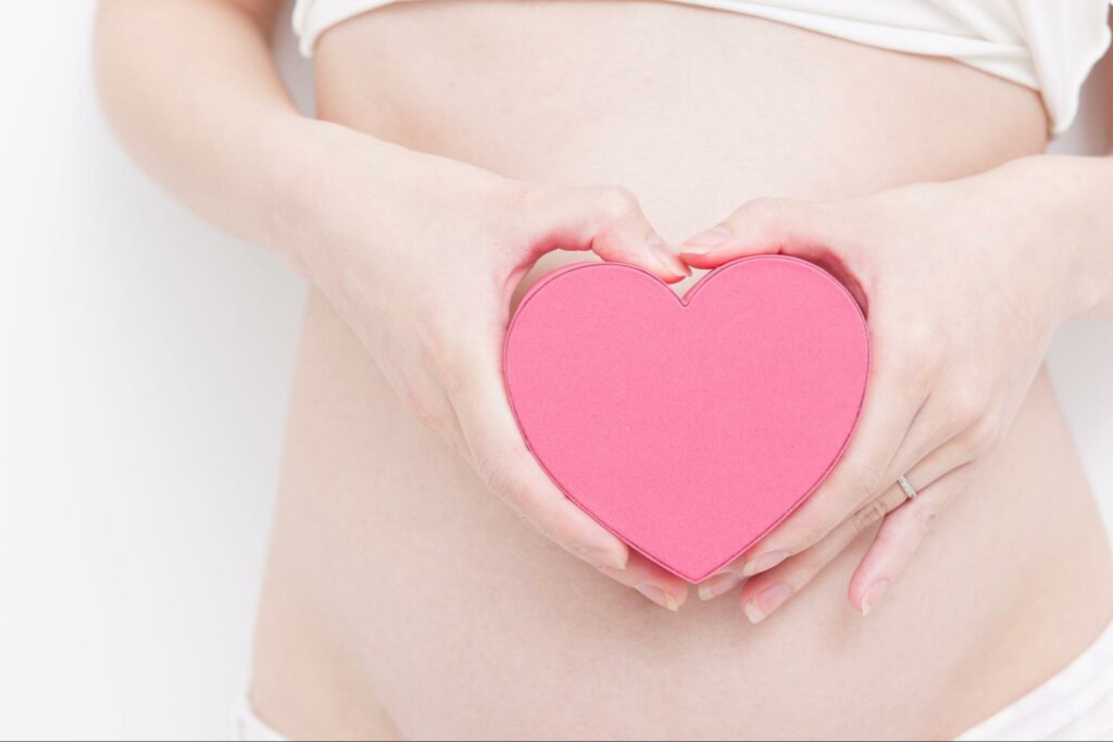 a woman holding a pink heart in front of her stomach to represent the connection between the gut and heart