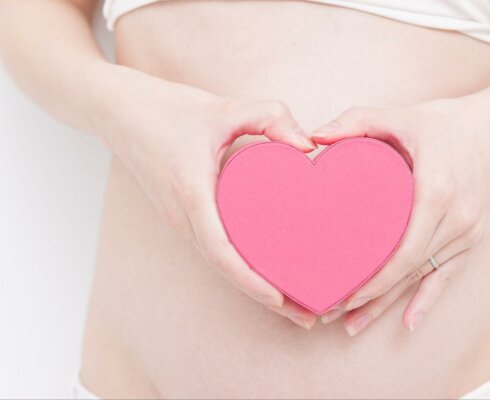 a woman holding a pink heart in front of her stomach to represent the connection between the gut and heart